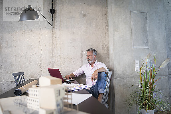 Geschäftsmann in einem Loft mit Laptop und Dokumenten und Architekturmodell auf dem Tisch