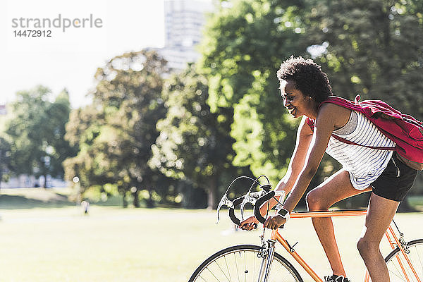 Lächelnde junge Frau fährt Fahrrad im Park