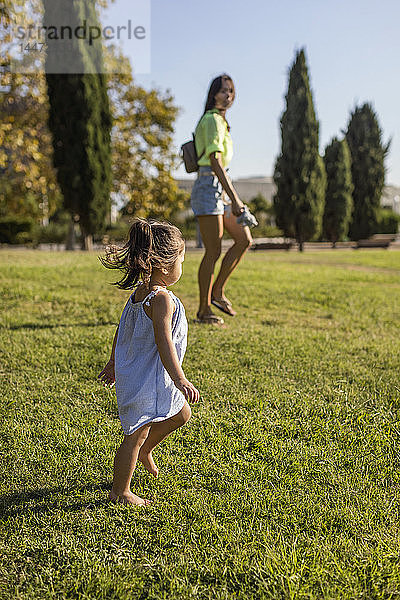 Kleines Mädchen  das mit seiner Mutter auf einem Rasen in einem Park spazieren geht