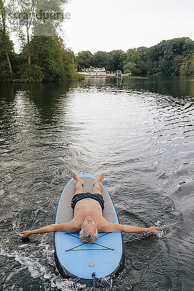 Älterer Mann liegt auf einem SUP-Brett auf einem See