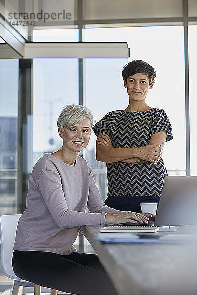 Porträt von zwei lächelnden Geschäftsfrauen mit Laptop am Schreibtisch im Büro