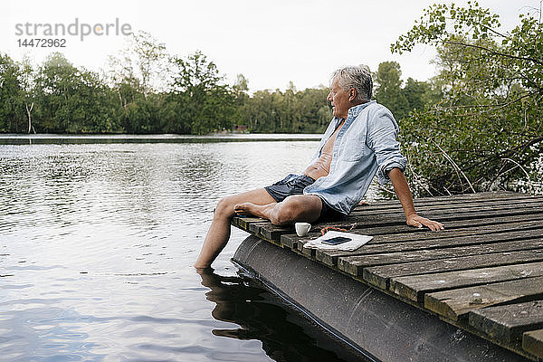 Älterer Mann sitzt auf einem Steg an einem See