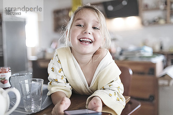 Porträt eines glücklichen kleinen Mädchens mit Smartphone in der Küche