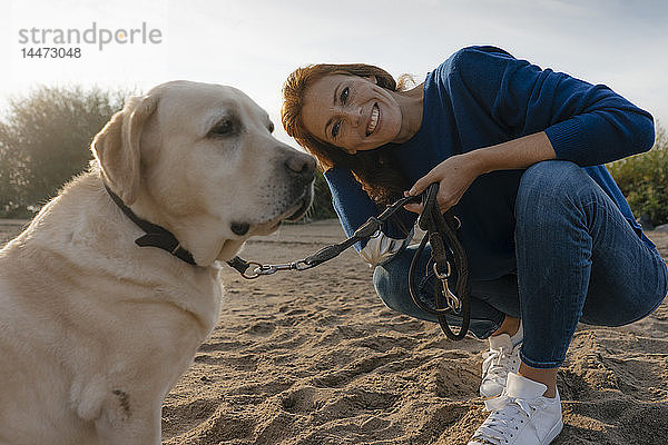 Deutschland  Hamburg  lächelnde Frau mit Hund am Strand am Elbufer