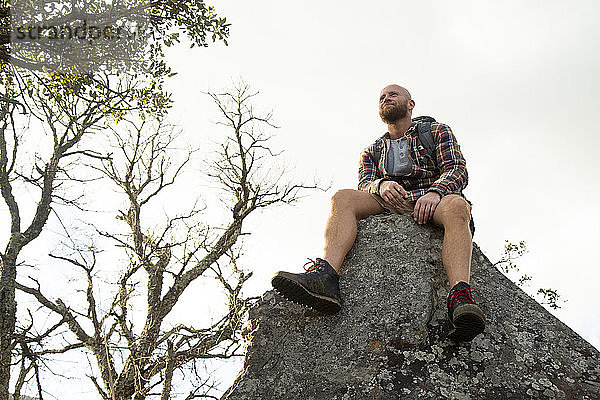 Spanien  Andalusien  Tarifa  lächelnder Mann auf einer Wanderung  der auf einem Felsen sitzend eine Pause macht