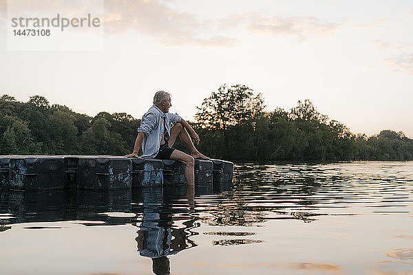 Älterer Mann sitzt bei Sonnenuntergang auf einem Floß in einem See