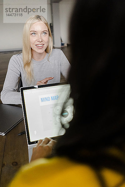 Zwei junge Geschäftsfrauen mit Laptop unterhalten sich am Konferenztisch im Büro
