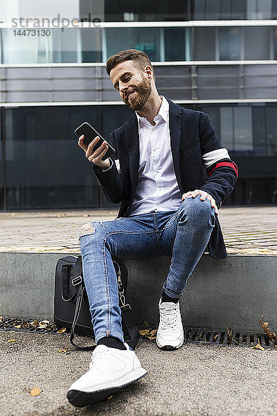 Stilvoller Geschäftsmann sitzt in der Stadt und benutzt sein Handy