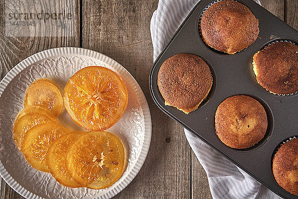 Kandierte Orangenscheiben auf Teller und Blech mit gebackenen Muffins