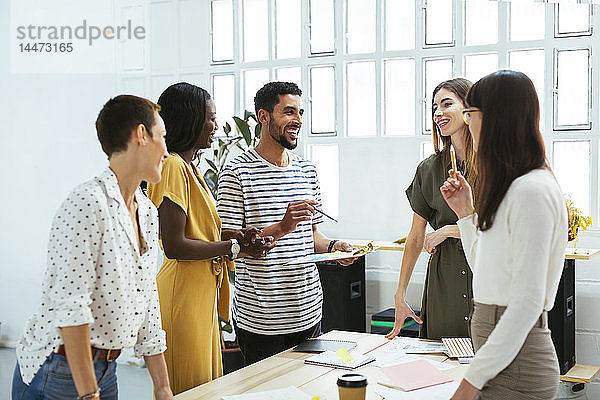 Lächelnde Kollegen arbeiten zusammen am Schreibtisch im Büro und diskutieren über Papiere