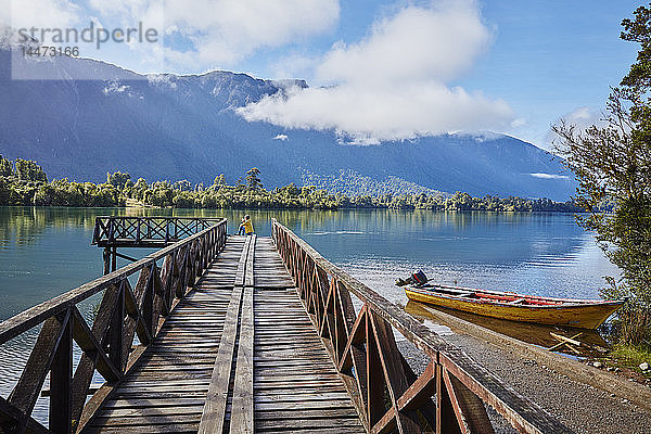 Chile  Chaiten  Lago Rosselot  Frau sitzt in der Ferne auf einem Steg