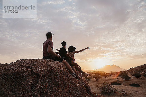 Namibia  Spitzkoppe  Freunde sitzen auf einem Felsen und beobachten den Sonnenuntergang