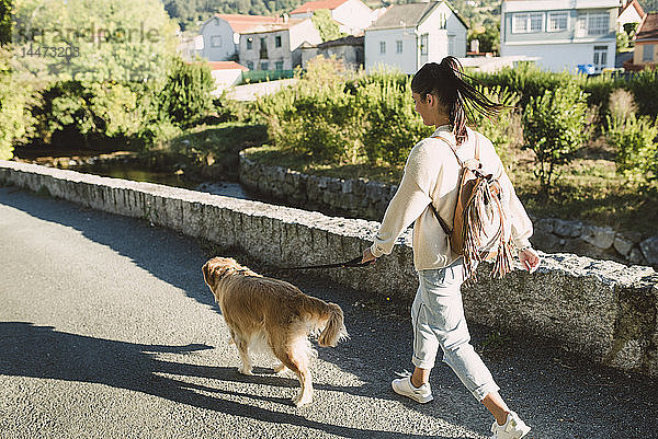 Frau geht mit ihrem Golden-Retriever-Hund auf einer Strasse spazieren
