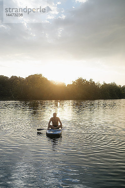 Älterer Mann sitzt bei Sonnenuntergang im SUP-Vorstand