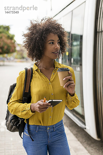 Porträt einer lächelnden Frau mit Kaffee zum Mitnehmen und Notizbuch in der Stadt