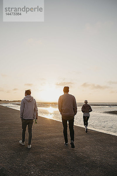 Namibia  Walvis Bay  Rückenansicht von drei Freunden  die bei Sonnenuntergang am Strand spazieren gehen