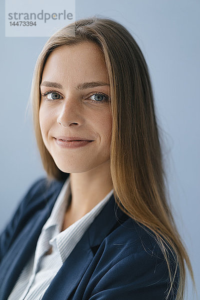 Porträt einer jungen Geschäftsfrau vor blauem Hintergrund  die selbstbewusst lächelt
