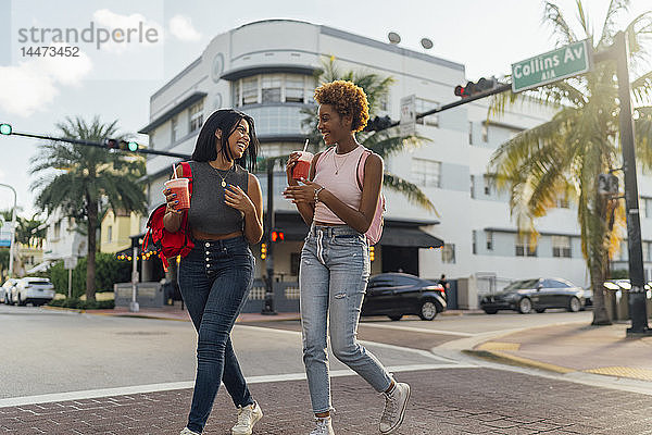 USA  Florida  Miami Beach  zwei glückliche Freundinnen bei einem Erfrischungsgetränk über die Straße