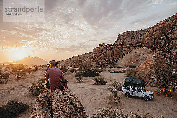 Namibia  Spitzkoppe  Freunde sitzen auf einem Felsen und beobachten den Sonnenuntergang
