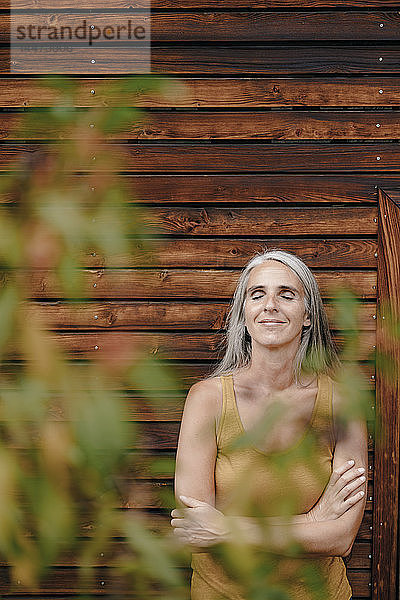 Porträt einer lächelnden reifen Frau  die vor einer Holzfassade steht