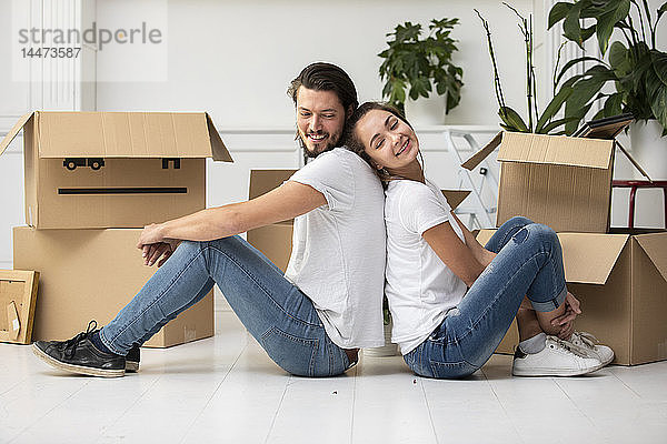 Glückliches Paar mit Pappkartons auf dem Boden sitzend in neuer Wohnung