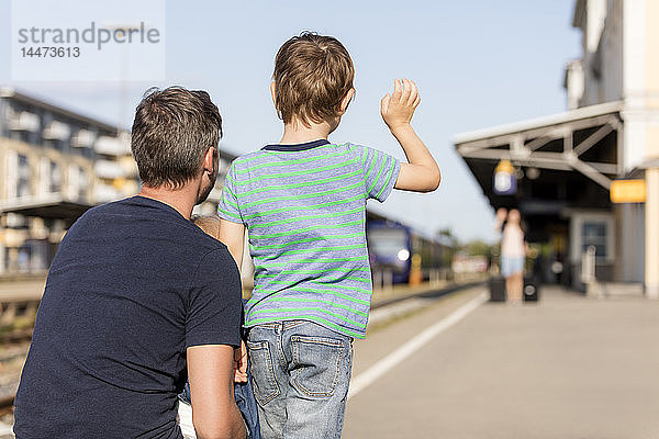 Sohn mit dem Vater winkt der Mutter auf dem Bahnsteig zu