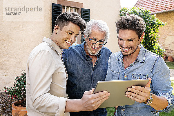 Drei glückliche Männer unterschiedlichen Alters mit Tablette im Garten