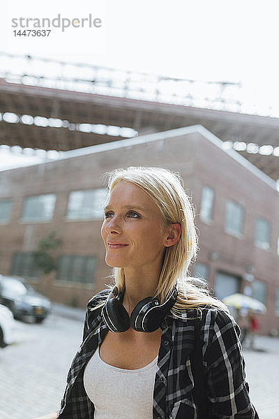 USA  New York City  Brooklyn  lächelnde junge Frau mit Kopfhörern in der Stadt