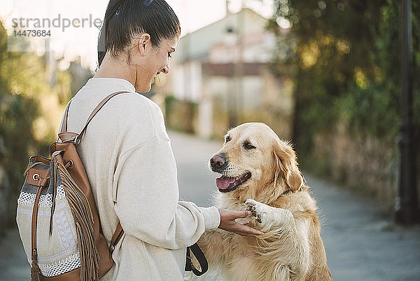Glückliche junge Frau spielt mit ihrem Golden-Retriever-Hund im Freien