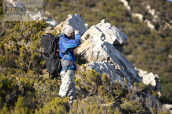 Spanien  Andalusien  Tarifa  Mann auf Wanderung in den Bergen beim Blick durchs Fernglas