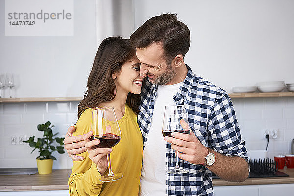 Glückliches Paar steht in der Küche  umarmt  trinkt Rotwein  küsst sich