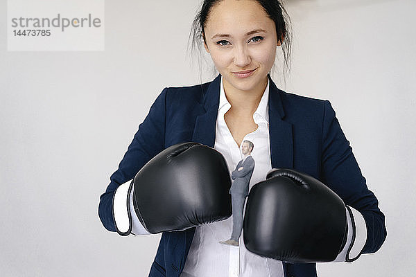 Geschäftsfrau hält Geschäftsmann-Figur zwischen Boxhandschuhen