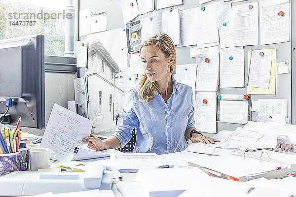 Frau sitzt am Schreibtisch im Büro und erledigt Papierkram