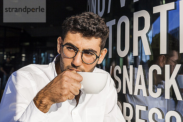 Porträt eines jungen Geschäftsmannes  der im Straßencafé Kaffee trinkt und etwas beobachtet