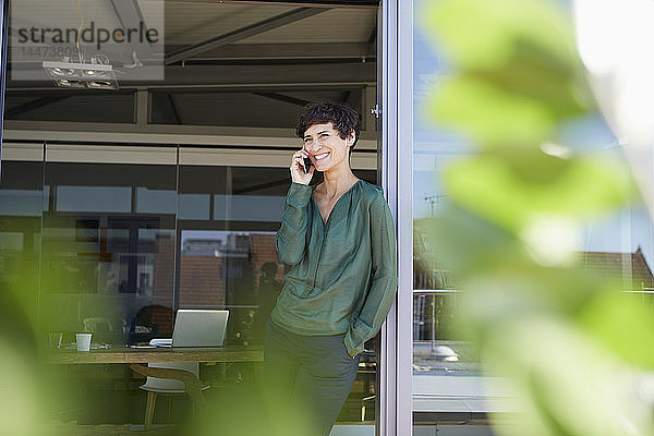 Lächelnde Frau steht am Fenster und telefoniert mit dem Handy
