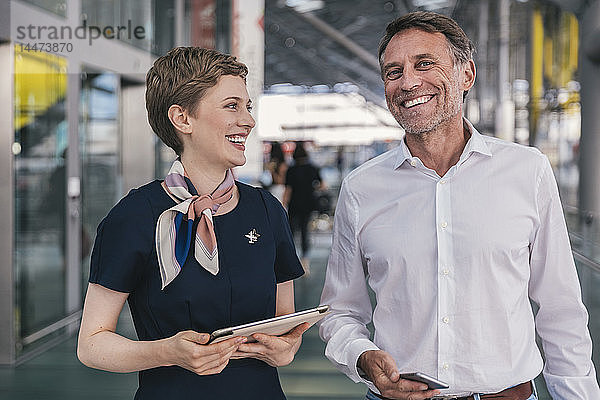 Glücklicher Fluglinienangestellter mit Tablette und Passagier mit Handy am Flughafen