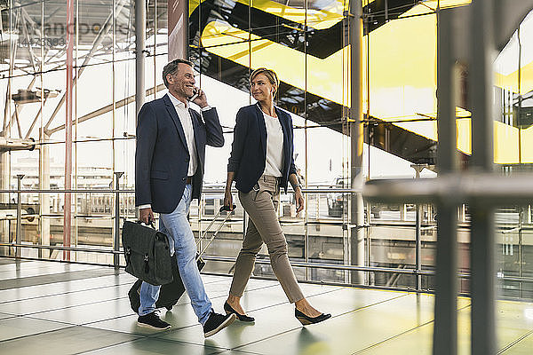 Geschäftsmann am Handy und Geschäftsfrau zu Fuß am Flughafen