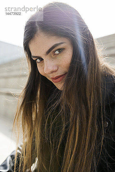 Porträt einer selbstbewussten jungen Frau mit langen braunen Haaren im Freien