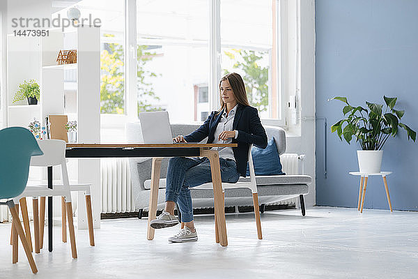 Junge Geschäftsfrau sitzt im Büro und benutzt Laptop
