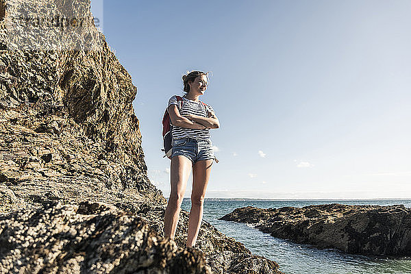 Junge Frau wandert an einem felsigen Strand und schaut sich die Aussicht an
