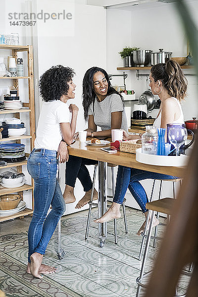 Drei glückliche Frauen unterhalten sich zu Hause am Küchentisch