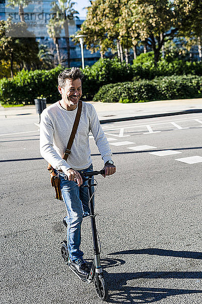 Erwachsener Mann  der mit seinem Kickroller in der Stadt unterwegs ist und eine Straße überquert