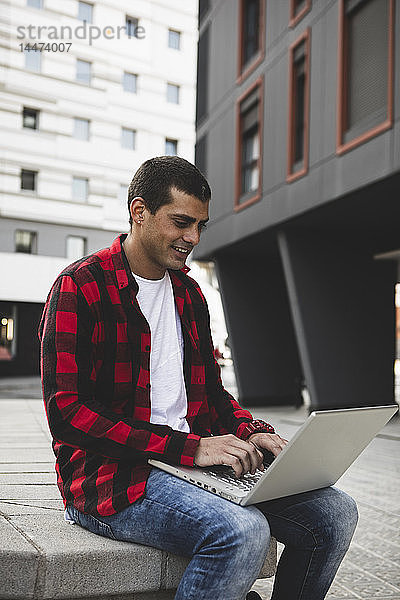 Junger Mann sitzt mit Laptop draußen in der Stadt