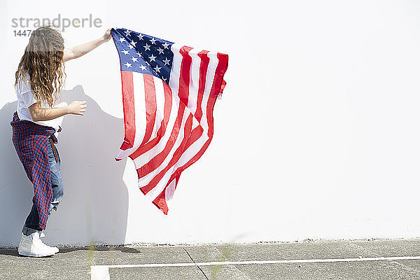 Mädchen hält amerikanische Flagge an weißer Wand