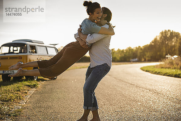 Glückliches Paar  das mit einem Wohnmobil unterwegs ist und sich auf der Straße umarmt