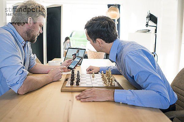 Zwei Männer spielen Schach und checken Smartphone