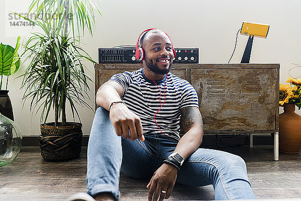 Lächelnder junger Mann mit Kopfhörern sitzt auf dem Boden in einem Loft