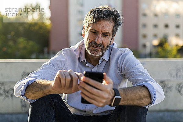 Reifer Mann sitzt in der Stadt und benutzt sein Handy