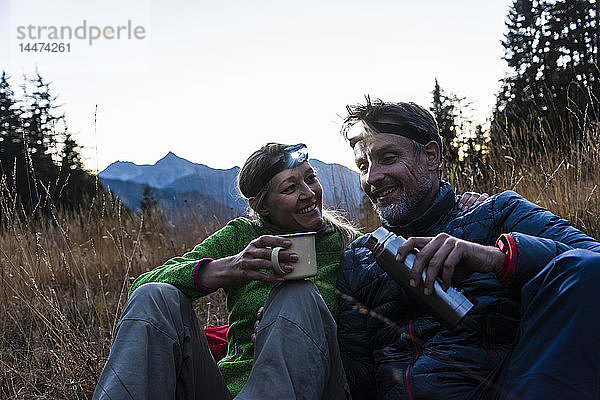 Wanderndes Ehepaar macht abends eine Pause  trägt Stirnlampen  trinkt Tee