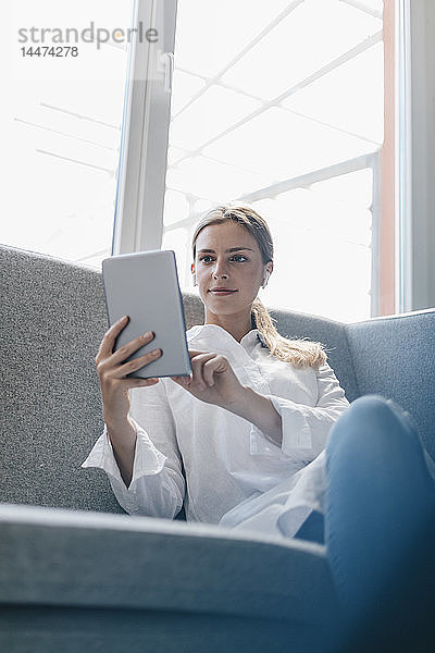 Junge Frau sitzt auf dem Sofa und benutzt ein digitales Tablett